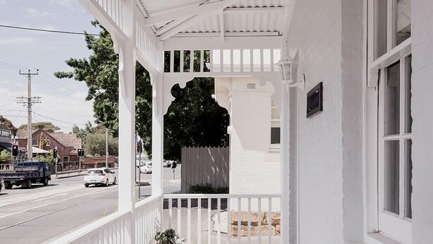 A covered porch with a wooden bench, a potted plant, and a view of the street.