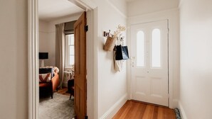 A hallway with a wooden floor, a white door, and a coat rack with hanging items.