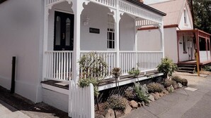 A white two-story house with a porch, a small garden, and a clear blue sky.