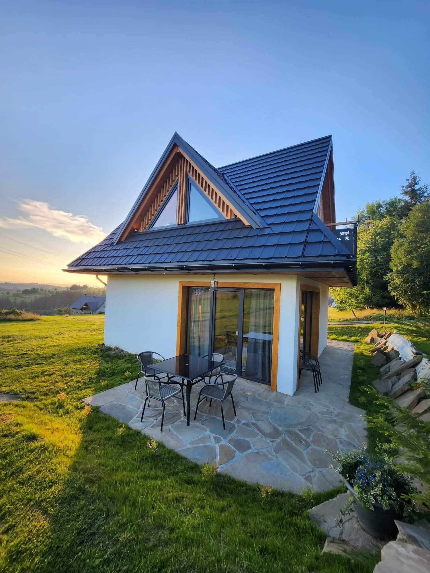 Une maison moderne avec un toit en pente, une terrasse en pierre et un coin repas aménagé avec du mobilier d’extérieur.