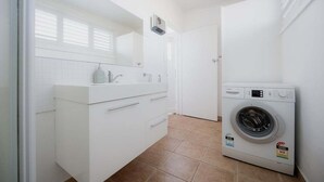 A laundry room with a washing machine, a white cabinet with drawers, and a tiled floor. - Mr Watson's Cottage in Battery Point (Battery Point)