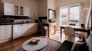 A modern kitchen with white cabinets, a dining area with a table and chairs, and a view of the city through large windows. - Central Hobart Studio (Hobart)