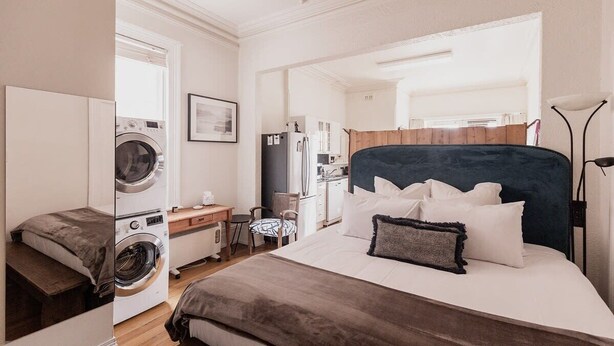 A hotel room with a bed, a washing machine, a desk, and a chair. - Central Hobart Studio (Hobart)