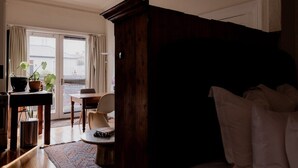 A room with a bed, a desk with a chair, a potted plant, and a window with curtains. - Central Hobart Studio (Hobart)