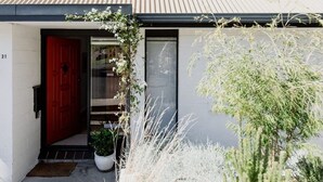 Una casa moderna con una puerta roja, un porche pequeño con una planta en maceta y una pared blanca.