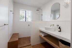 Une salle de bain moderne avec des carreaux blancs, une douche, un lavabo avec un miroir et une fenêtre.