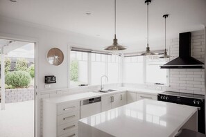 A modern kitchen with white cabinetry, a large island, pendant lighting, and a black range hood. - Beautiful three bedroom period house in Sandy Bay (Sandy Bay)