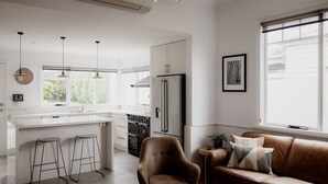A modern kitchen with a central island, bar stools, a brown leather sofa, and a large window with a view.