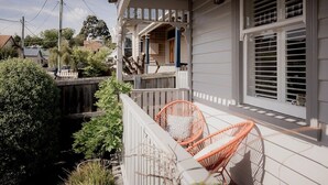 A porch with white railings, a wooden deck, and two wicker chairs.