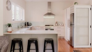 A modern kitchen with a central island, a stove, a sink, and a refrigerator. There are three stools at the island and a clock on the wall. - Modern Home in Sandy Bay - Sleeps 8 Guests (Sandy Bay)