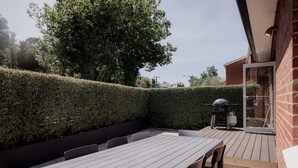 An outdoor patio with a table and chairs, a barbecue grill, and a neatly trimmed hedge. - Modern Home in Sandy Bay - Sleeps 8 Guests (Sandy Bay)
