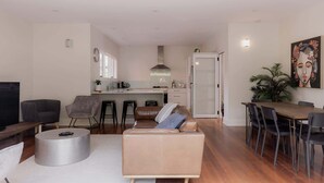 A modern living room with a sofa, coffee table, and TV. A kitchen is visible in the background with a dining area and chairs. - Modern Home in Sandy Bay - Sleeps 8 Guests (Sandy Bay)
