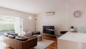 A modern living room with a leather sofa, a round ottoman, a flat-screen TV, and a minimalist coffee table. - Modern Home in Sandy Bay - Sleeps 8 Guests (Sandy Bay)