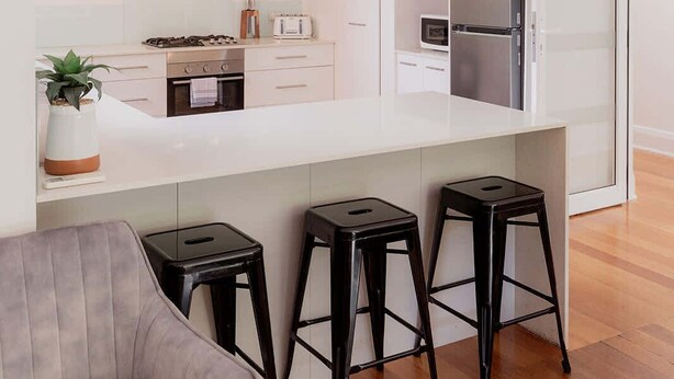 A modern kitchen with a central island, bar stools, and a grey upholstered chair. - Modern Home in Sandy Bay - Sleeps 8 Guests (Sandy Bay)