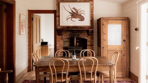 A dining area with a wooden table and chairs, a brick fireplace, and a framed picture above the fireplace. - Maple House - Charming family cottage in Sandy Bay (Sandy Bay)