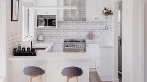 A modern kitchen with white cabinetry, a central island with stools, a built-in oven, and a microwave. - Modern refurbished unit in charming Bellerive (Bellerive)
