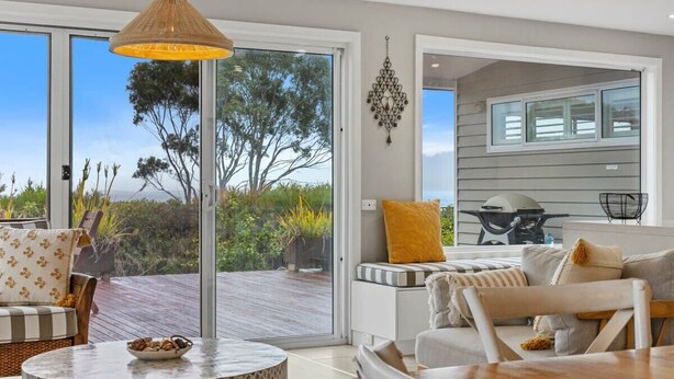 A modern living room with a large sliding glass door leading to an outdoor deck, a round table with a bowl, and a hanging light fixture.