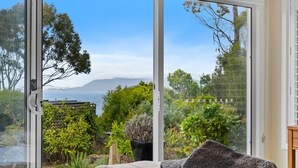 A bedroom with a large sliding glass door leading to a garden with a view of the sea and mountains.