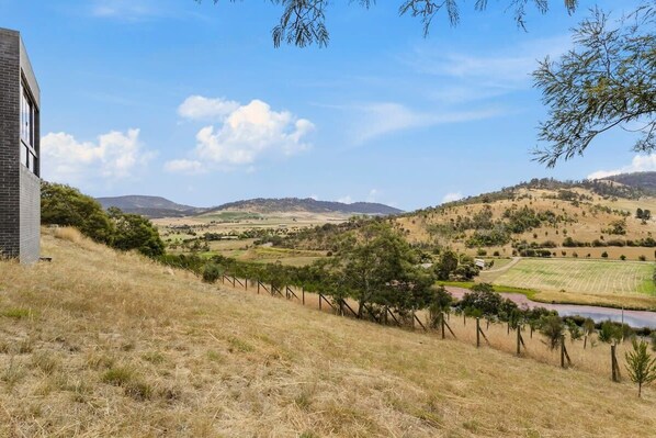 A rural landscape with a building on a hillside, fields, and a river.