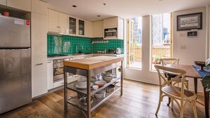 A modern kitchen with a wooden island, stainless steel appliances, and a green tiled backsplash. - Deco Loft on Russell Street (Melbourne)