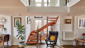 A spacious living area with a wooden staircase, a black leather chair, and a potted plant. - Deco Loft on Russell Street (Melbourne)