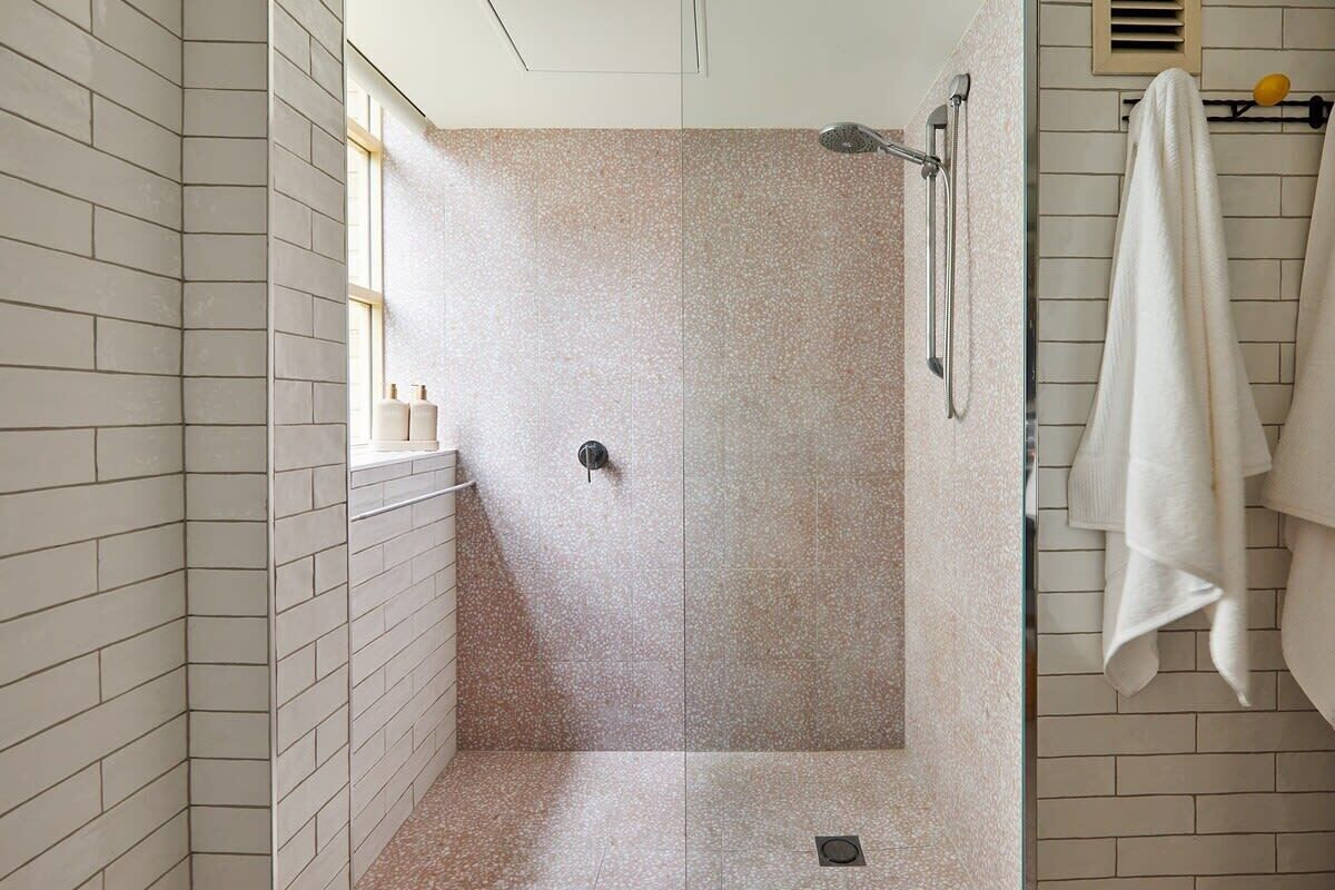 A shower with a glass door, a towel rack, and a window on the left side.