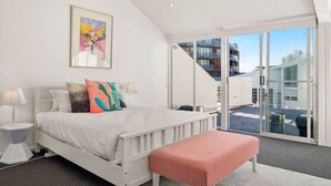 Une chambre à coucher avec un lit, un banc, une table de chevet et un tableau accroché au mur.