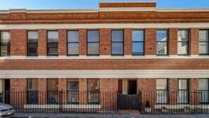 Un bâtiment à deux étages, dot é d’une façade en briques, de nombreuses fenêtres et d’une entrée fermée par un portail.