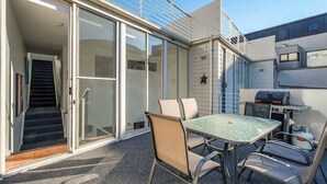 Une terrasse extérieure avec une table et des chaises, un barbecue et une porte-fenêtre coulissante donnant sur un escalier.