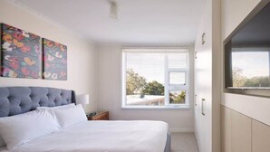 Une chambre à coucher avec un grand lit, une fenêtre avec des stores, une œuvre d’art accrochée au mur et une armoire.