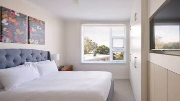 A bedroom with a large bed, a window with blinds, a wall-mounted artwork, and a wardrobe.
