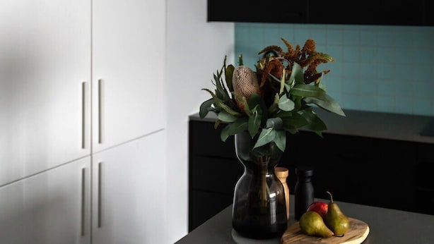 A modern kitchen with white cabinets, a black countertop, and a vase with dried flowers and fruits. - Sayer Gardens Apartment (Sandy Bay)