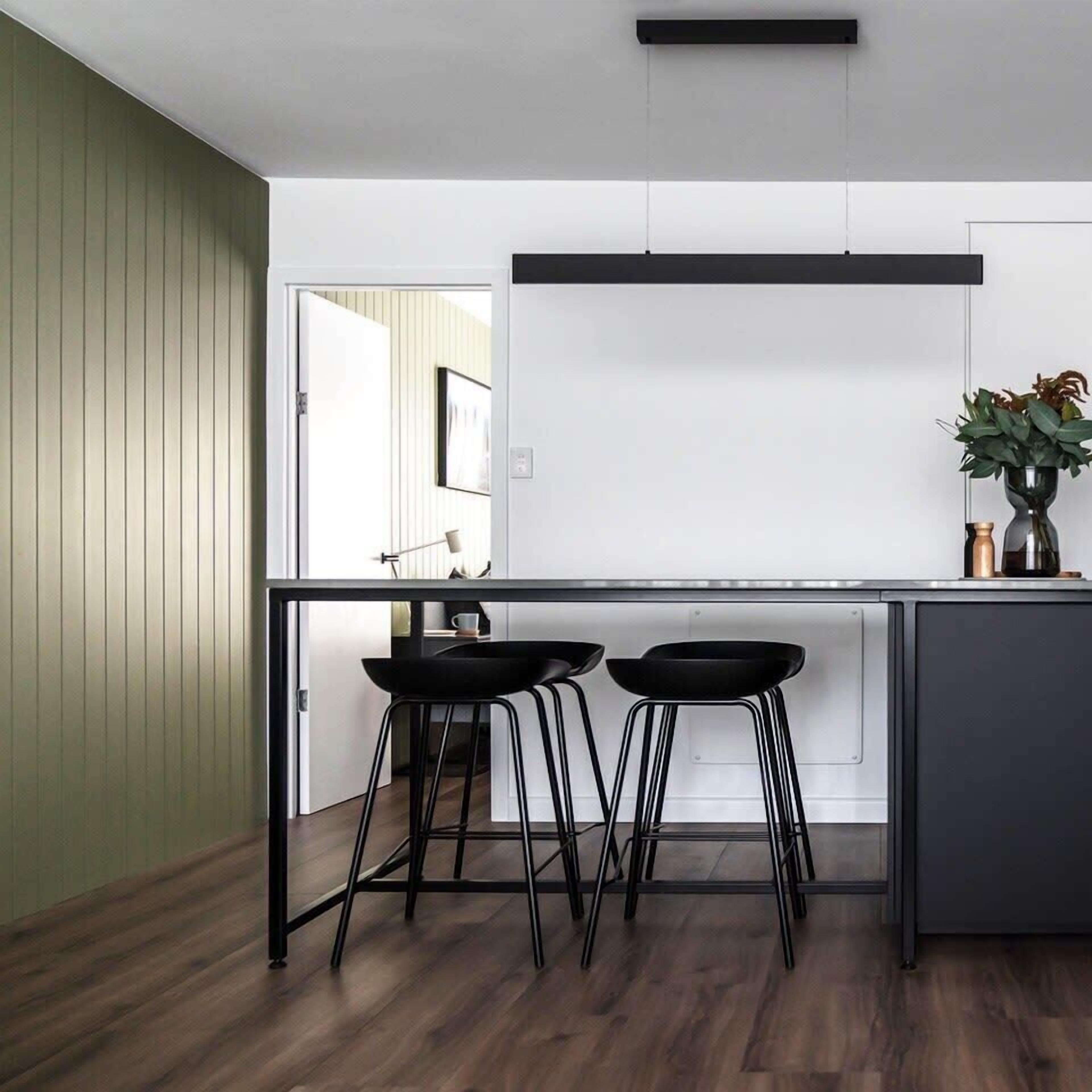 A modern kitchen with a black countertop, two black stools, and a potted plant on the island.