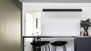 A modern kitchen with a black countertop, two black stools, and a potted plant on the island. - Sayer Gardens Apartment (Sandy Bay)