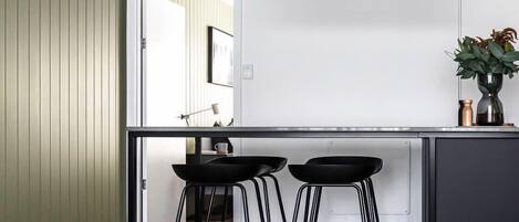 A modern kitchen with a black countertop, two black stools, and a potted plant on the island.