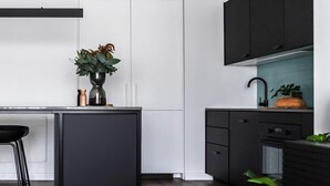 A modern kitchen with dark cabinetry, a white door, and a wooden floor. - Sayer Gardens Apartment (Sandy Bay)