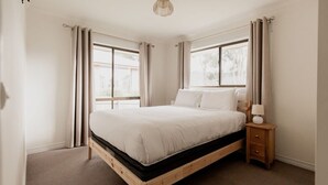 Un dormitorio con cama de madera, una mesita de noche y una ventana con cortinas.