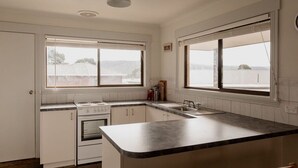Una cocina con alacenas blancas, una estufa y un lavamanos. Hay dos ventanas que ofrecen vistas al exterior.