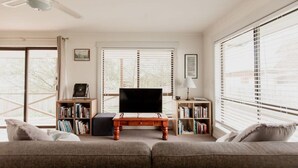 Una sala de estar con un sofá, un televisor sobre un mueble de madera y estanterías llenas de libros.