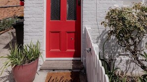 A red door with a mailbox, a white picket fence, and a welcome mat. - Stay steps from Salamanca in historical cottage (Battery Point)