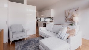 A modern living room with a grey armchair, a white sofa with multiple cushions, and a patterned rug. - Stay steps from Salamanca in historical cottage (Battery Point)