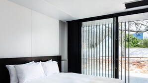 A modern hotel room with a large bed, a black headboard, and a view of the outdoors through a sliding glass door. - The Conservatory Summ (Hobart)
