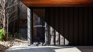 A modern building with a wooden slatted roof, a glass door entrance, and a gravel pathway leading to it. - The Conservatory Summ (Hobart)