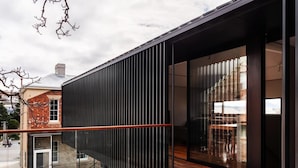 A modern building with a glass facade, a wooden deck, and a metal railing. - The Conservatory Summ (Hobart)