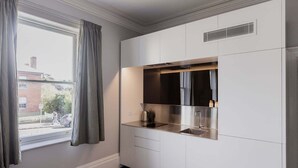 Una cocina moderna con armarios blancos, una campana extractora de acero inoxidable y un ventanal con cortinas.