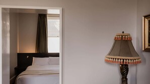 Una habitación de hotel con cama, mesita de noche, lámpara y ventana con cortinas.