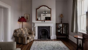 A traditional living room with a fireplace, a red lamp, a patterned rug, and a mirror above the mantel. - The Parlour Summary: (Hobart)