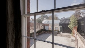 A view through a window of a courtyard with a brick wall, a metal fence, and a building with a sloped roof. - The Parlour Summary: (Hobart)