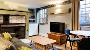 Een ruimtelijke woonkamer met kitchenette, televisie, bank en eettafel.