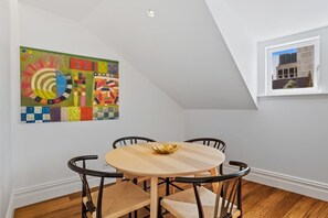 A dining area with a round table and four chairs, a colorful abstract painting on the wall, and a window with a view of a building. - Historical Victoria Tavern Three (Hobart)